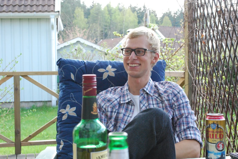 a man sits in an outdoor chair with three alcohol bottles next to him