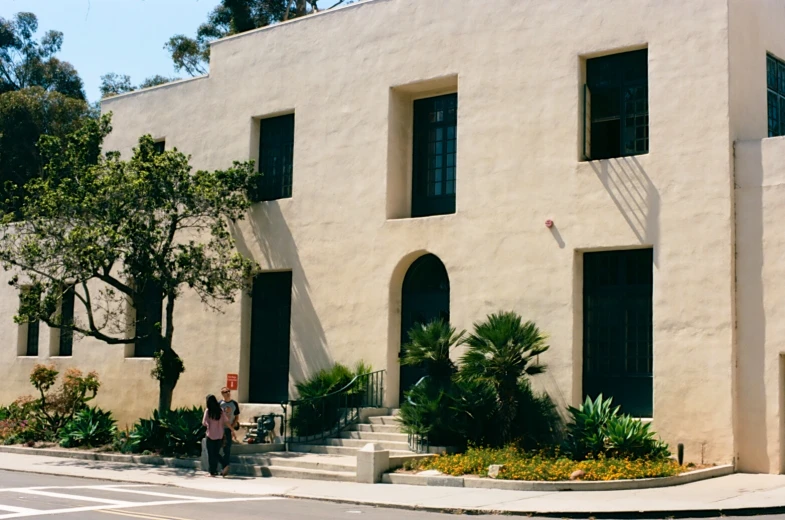 a building has two people standing outside and bushes