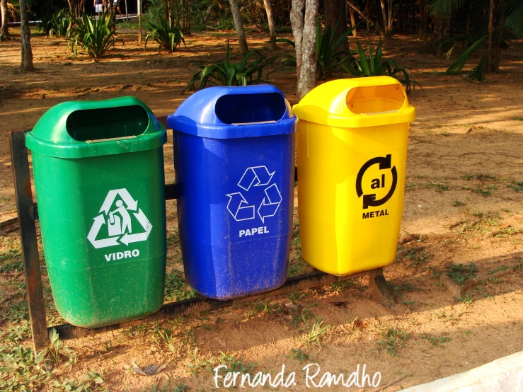 three trash can sitting in the dirt in front of trees