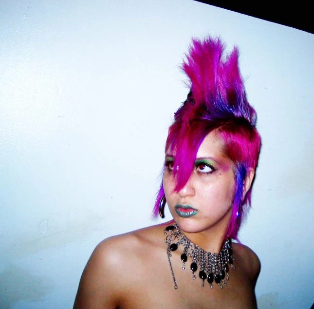 a girl with pink hair and piercings stands near a wall