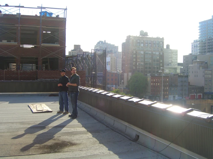 two people standing on a roof in front of a tall city