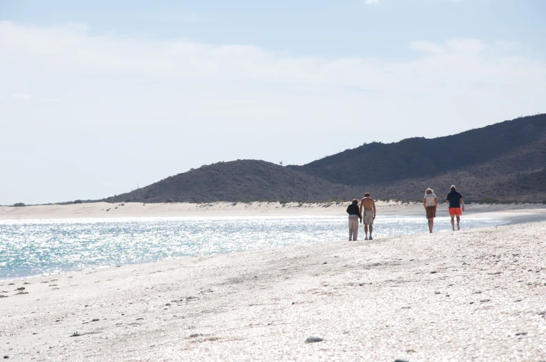 three people standing on the beach near a lake