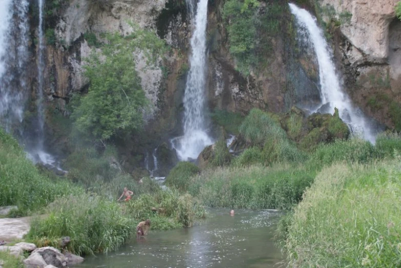 three people bathing in the water by a waterfall