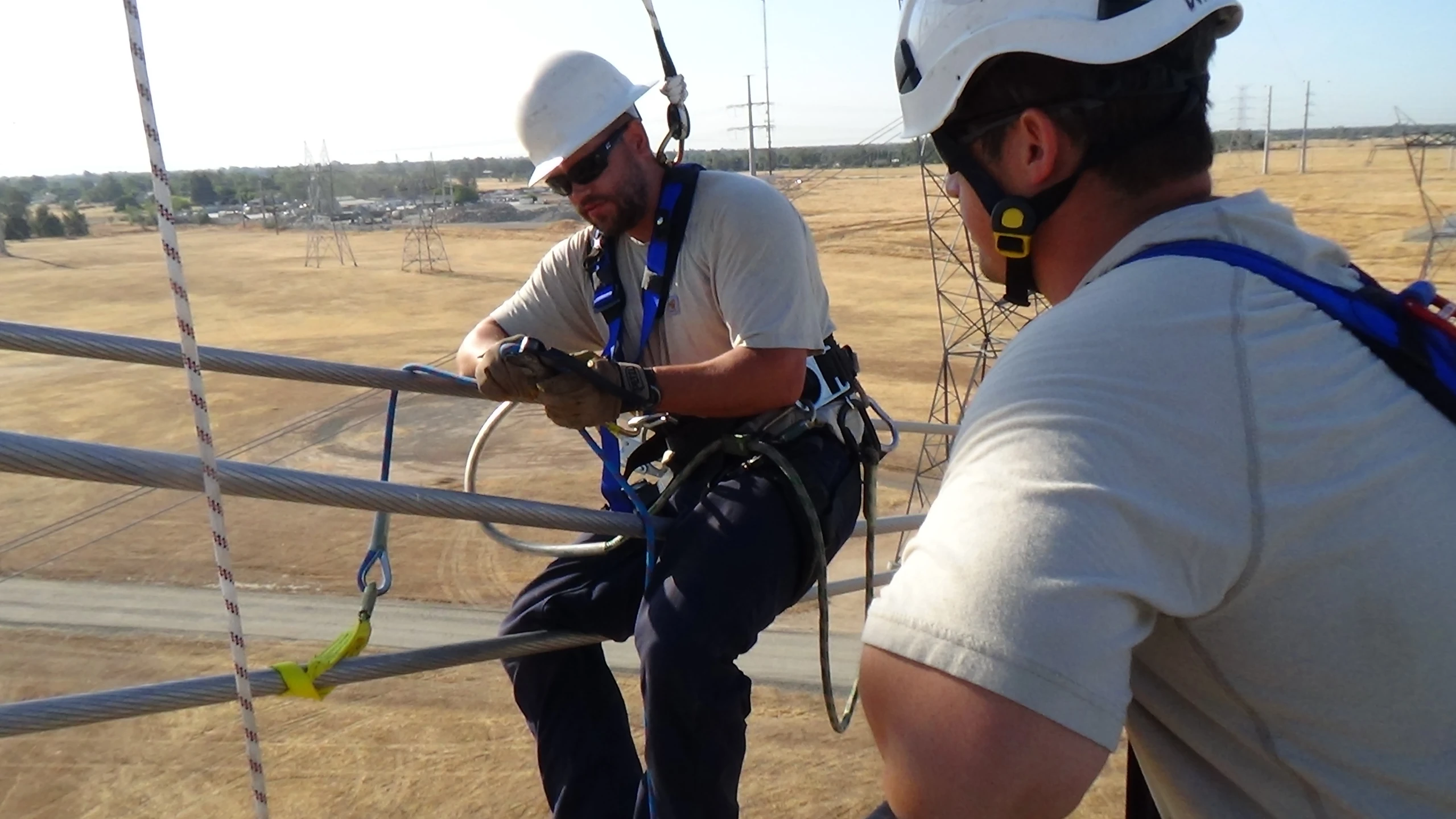 two workers in hard hats climbing up the side of a metal railing