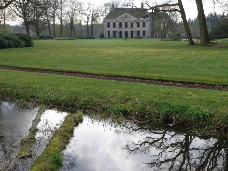 a large house near a small stream on top of a green field