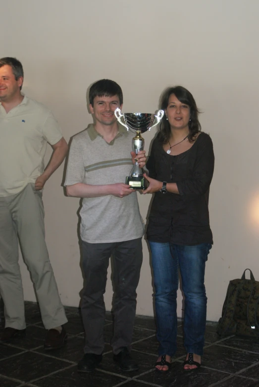 two men and a woman standing with a trophy
