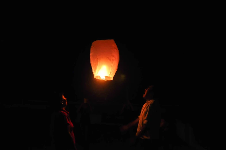 three people standing around a lit up sky lantern