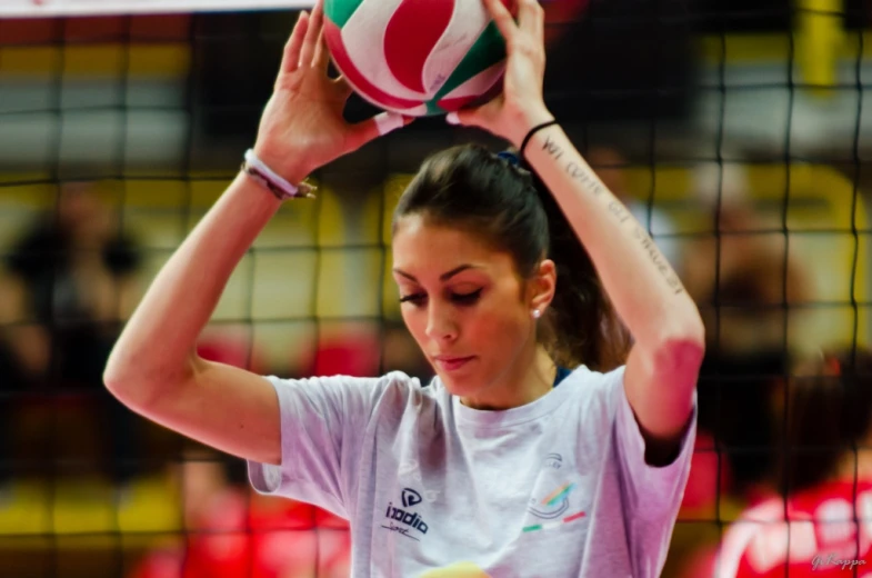 a woman in grey shirt holding a volleyball over her head