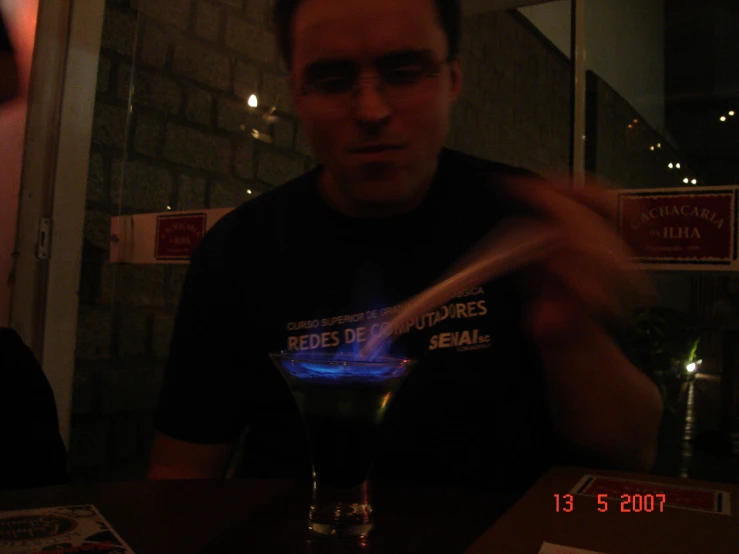 man standing at a bar pulling on a blue liquid in his glass