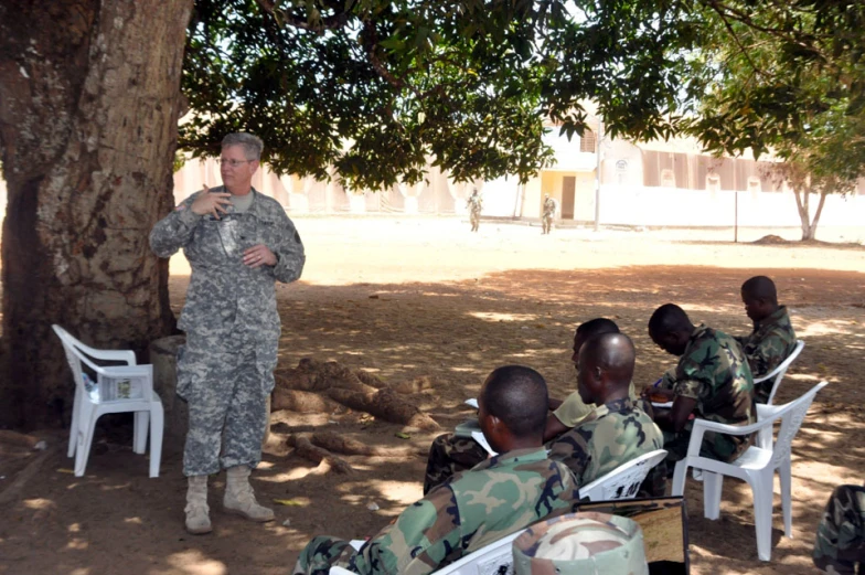 a soldier speaks to young men under a tree