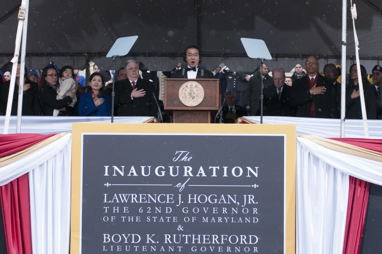 a man speaking at a podium while surrounded by people