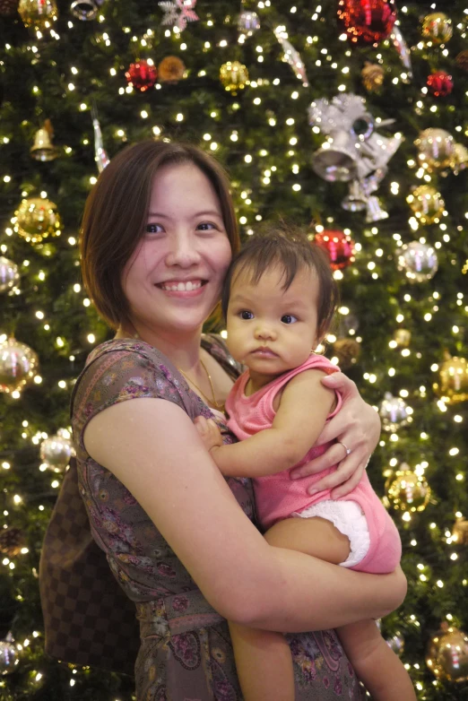 woman smiling holding baby in front of christmas tree