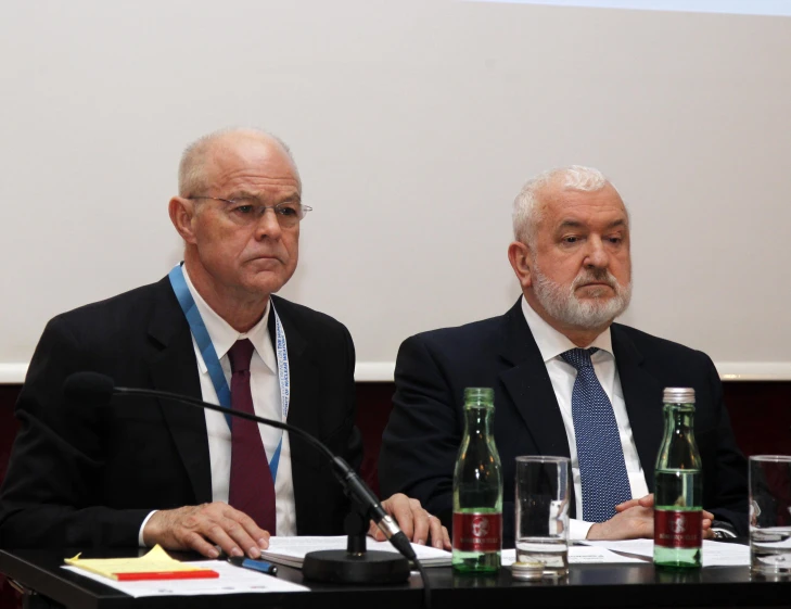 two men sitting at a table speaking with other people