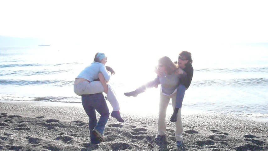 three women are on a beach and one of them is carrying a child in her arms