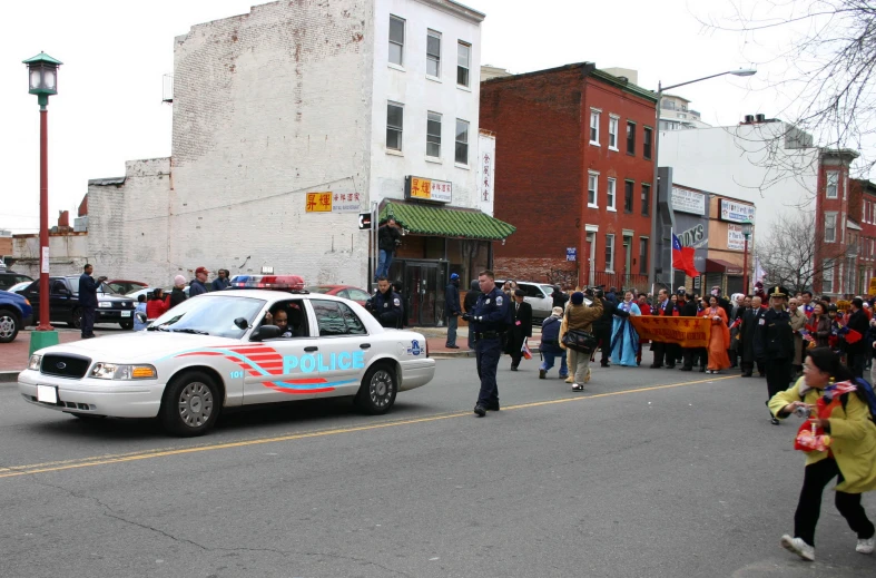 people and police car driving on the street during a parade