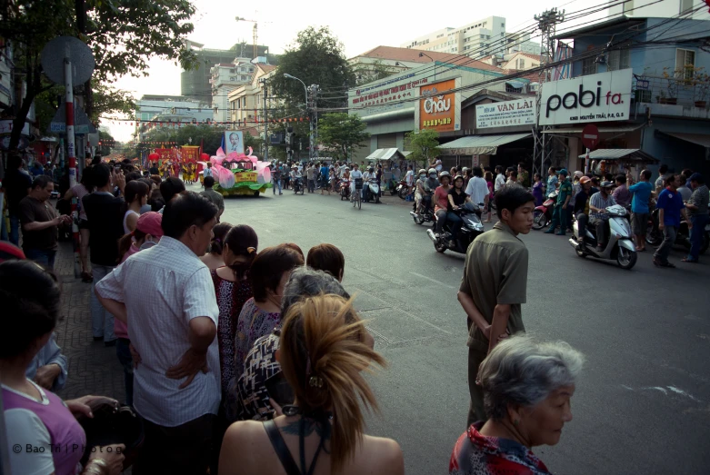 large group of people walking on a street with a man riding a motor scooter in the background