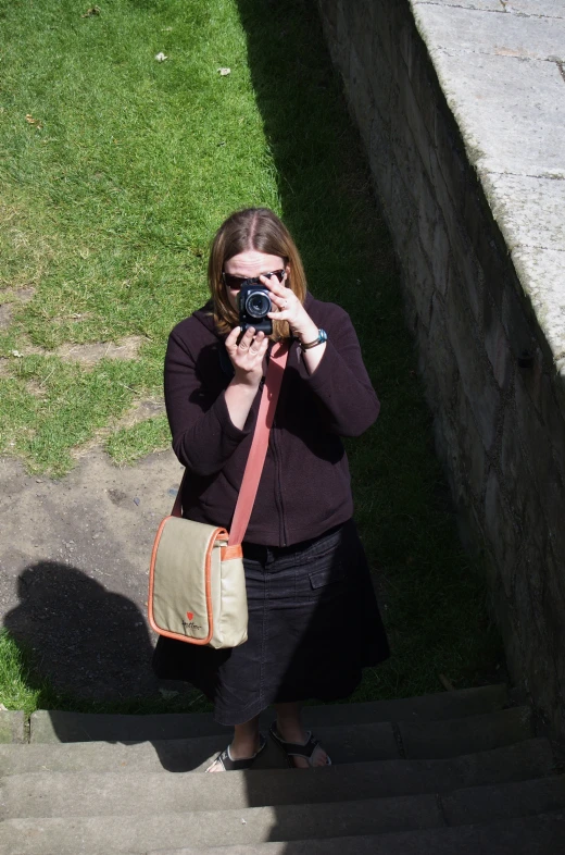 a woman in a black top is standing with a brown bag and holding a camera