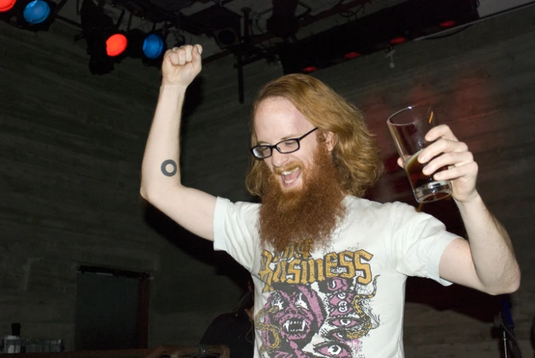 a bearded man with a red, orange and black shirt holds up a drink in his hand