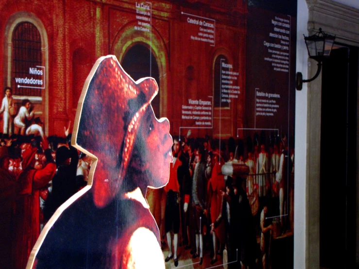 a man in a red hat standing next to a wall with pictures of people