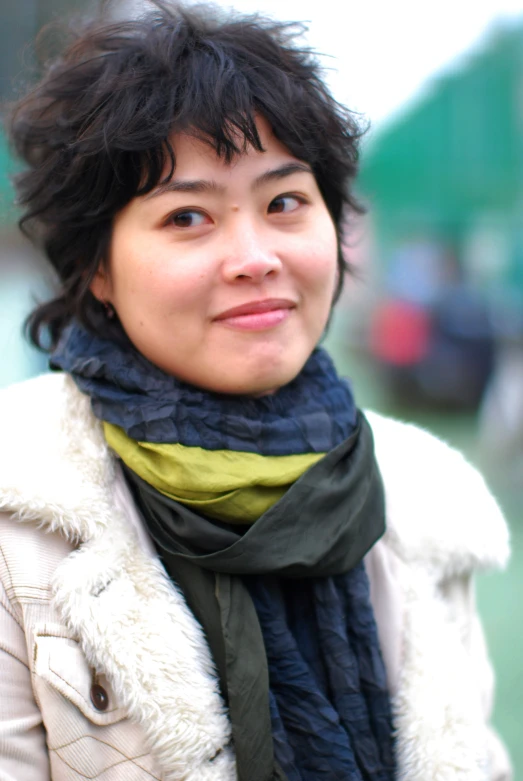 a woman with short hair wearing a green scarf and a white coat