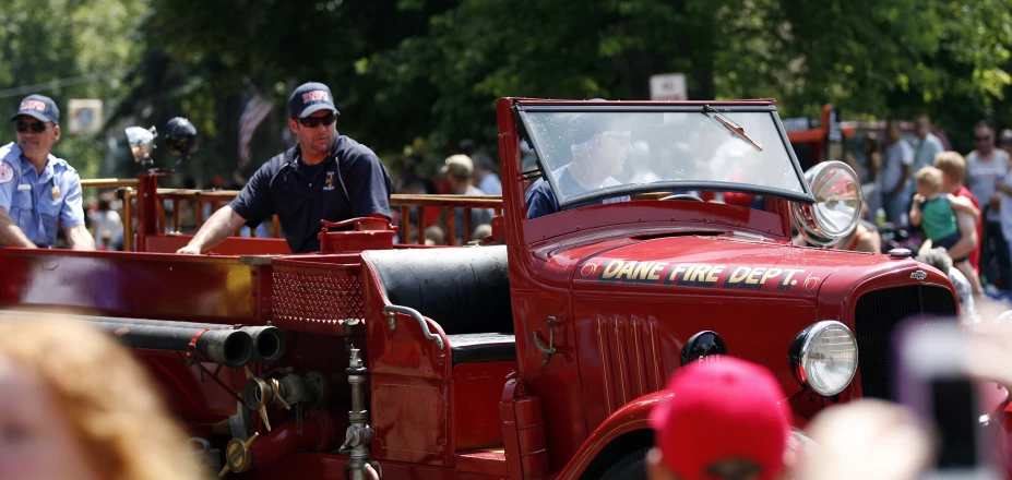 a group of people standing near and looking at an old red truck