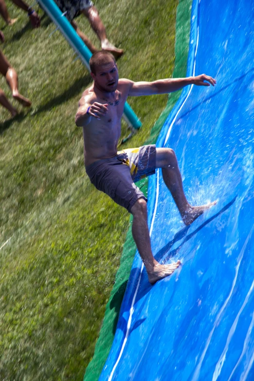 a man that is riding a water slide in the grass