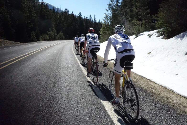 a couple of men riding on the backs of bikes down a snow covered road