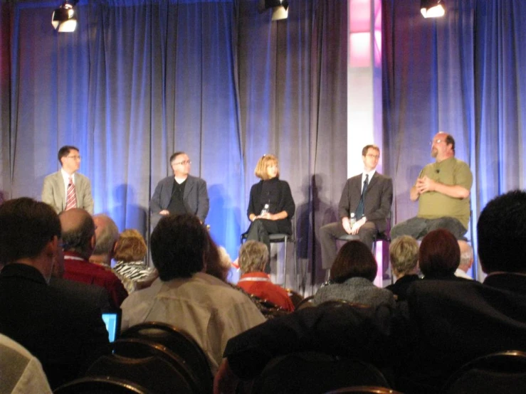 four people on stage, sitting down talking to other people