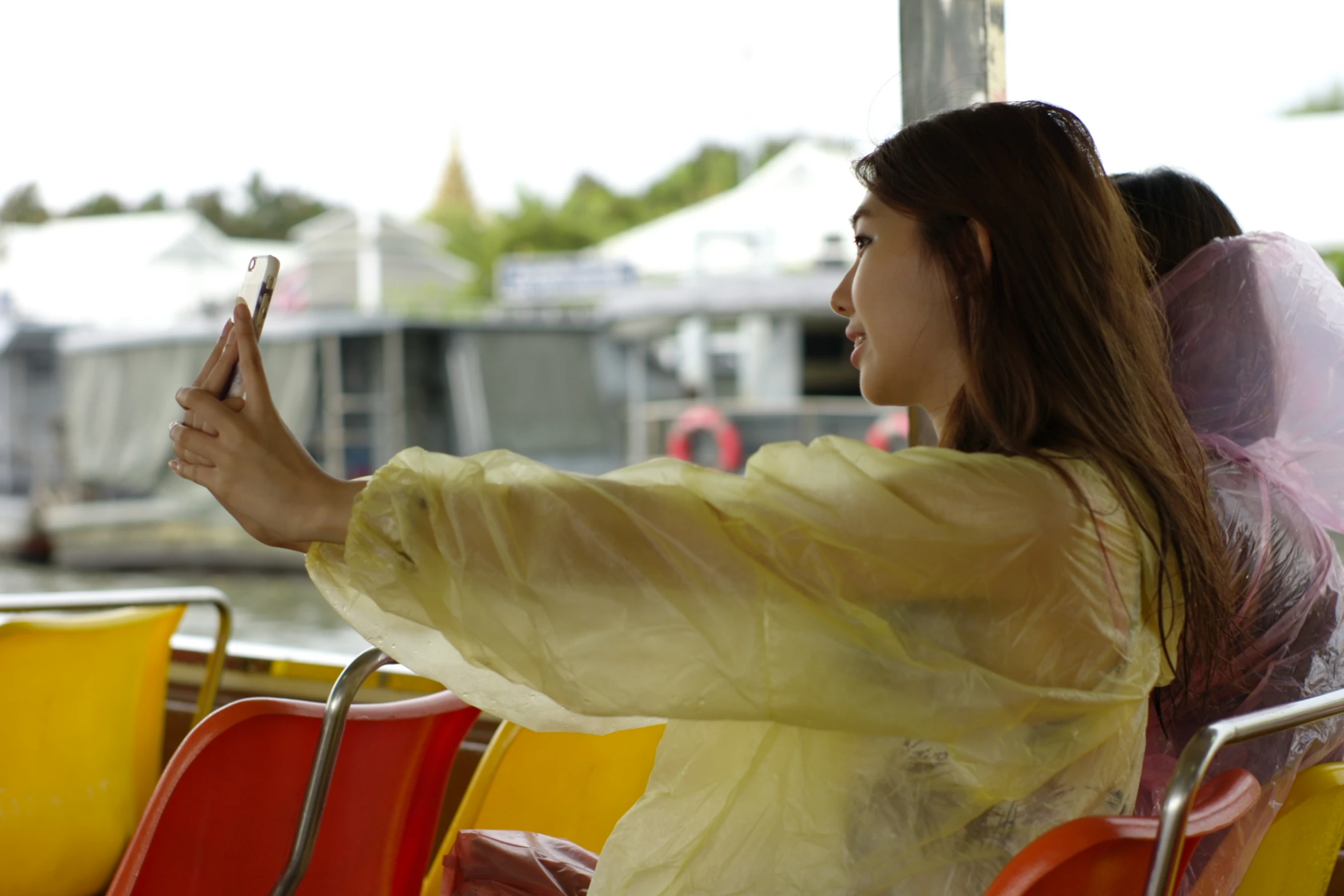 an asian woman holding her phone and wearing a raincoat