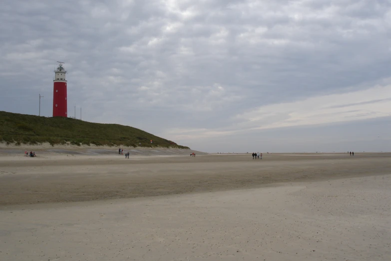 several people are walking on the sand near a large red light house