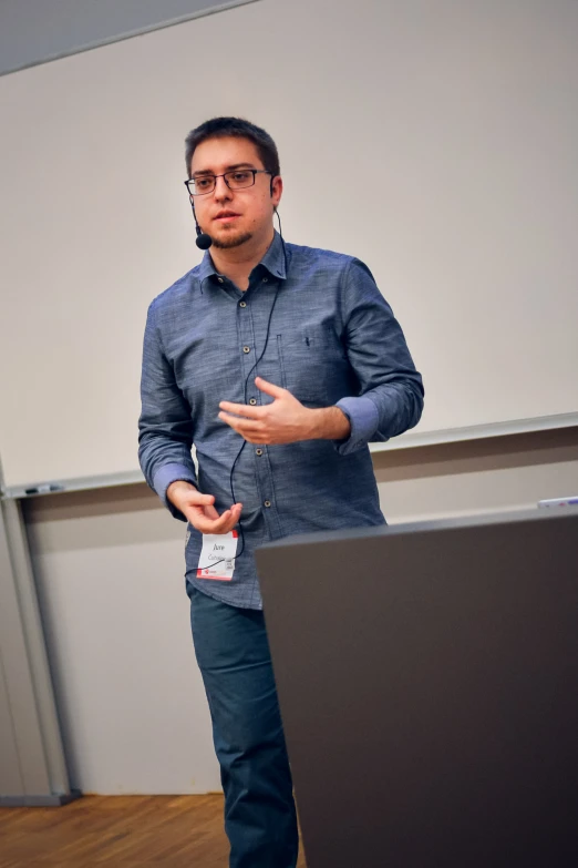 a man with eye glasses standing next to a laptop