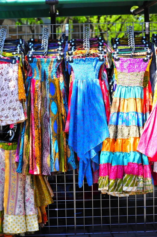 dresses hanging outside on racks by a fence