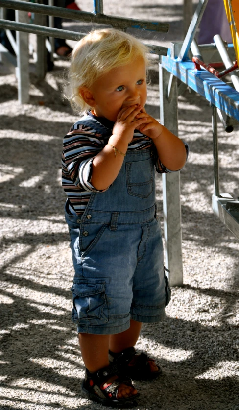 a little boy wearing a blue dungks and a blue shirt eating soing off his hand