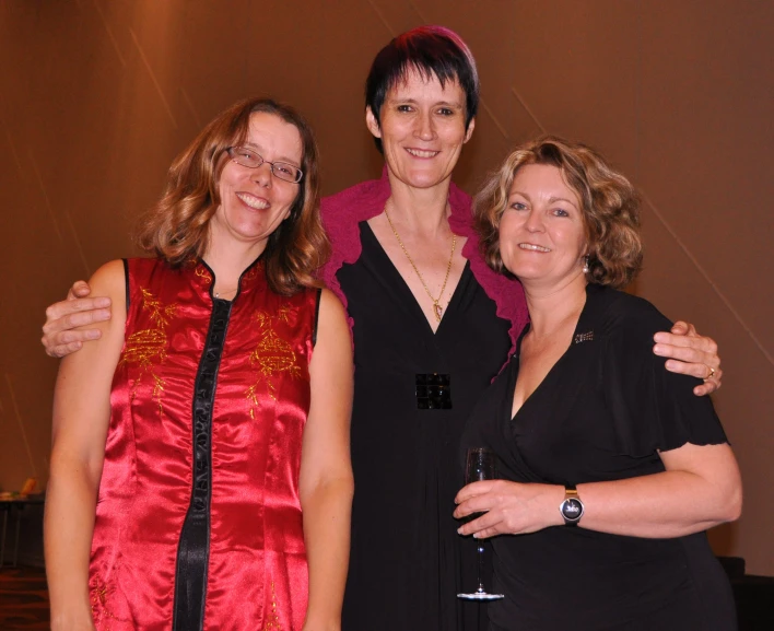 three women smile together with one arm around the other