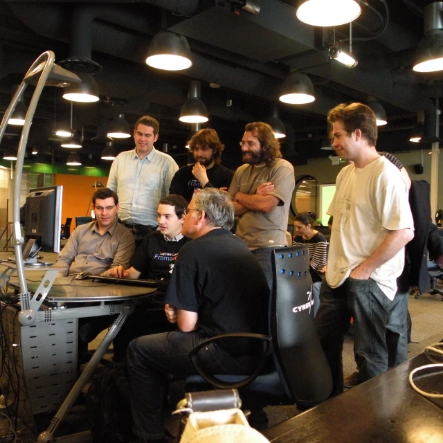 group of men stand around a computer in an office