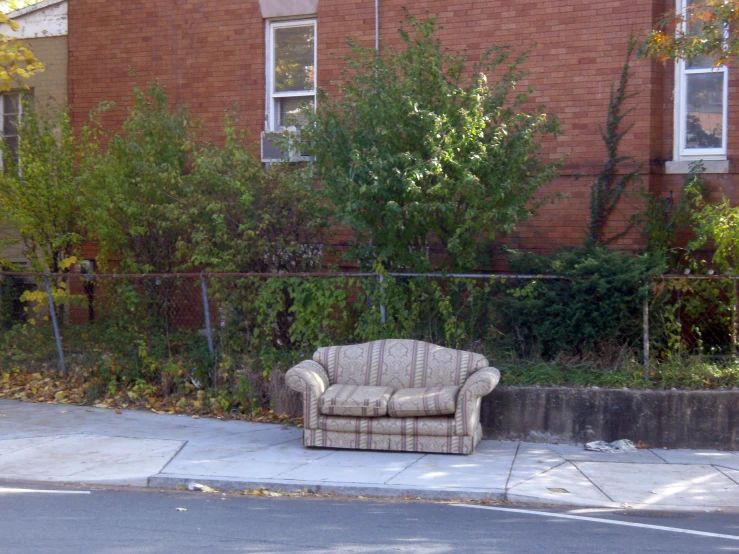 a couch sits on the side of a sidewalk next to an abandoned house