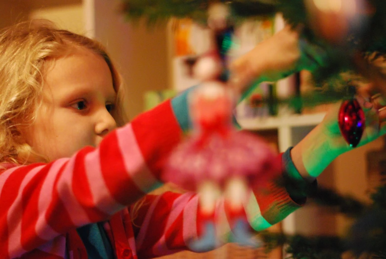 a small girl is putting the first ornament on a tree