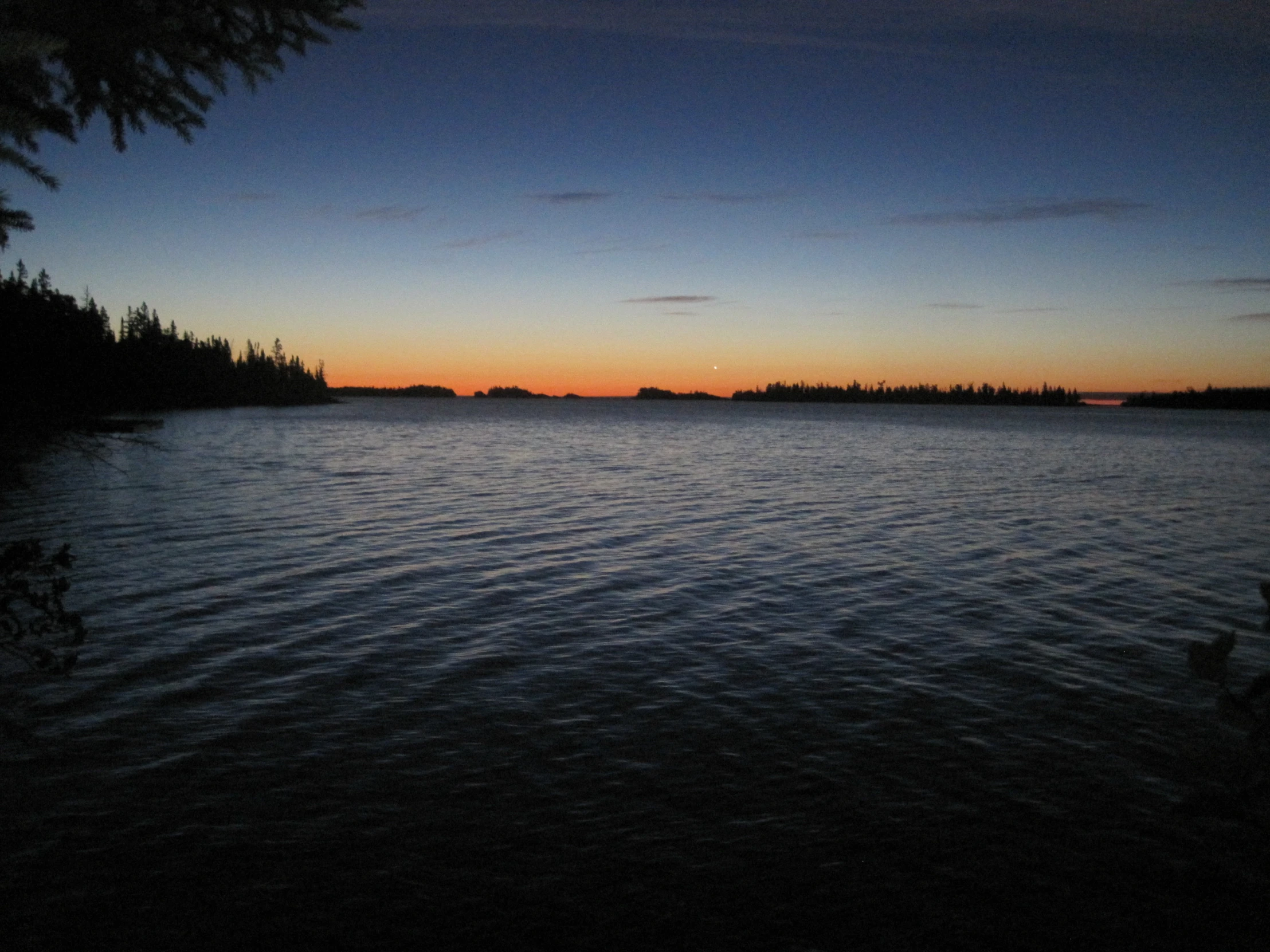 a sunset over the ocean with trees on the shore