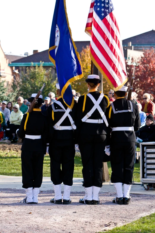 a group of people watching men in black uniforms march with flags