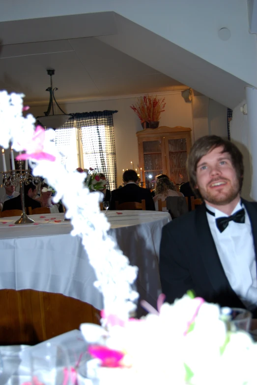 a young man dressed in black sits with another at a dinner table