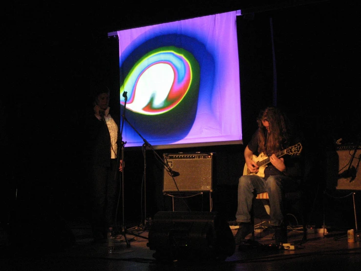 a man sitting on stage while playing a guitar