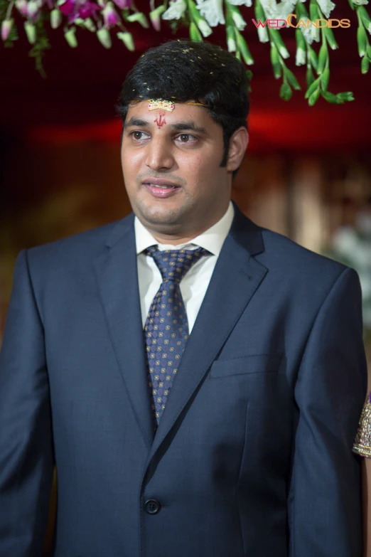 a young man in a suit standing beneath flower leis