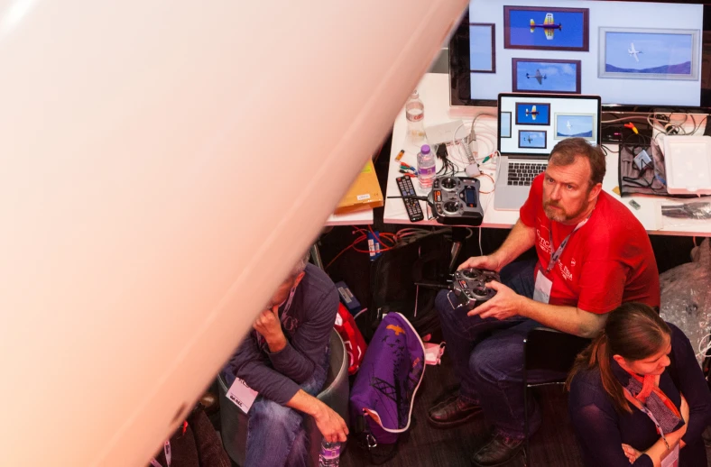 three people sitting around a table with electronics on the desk