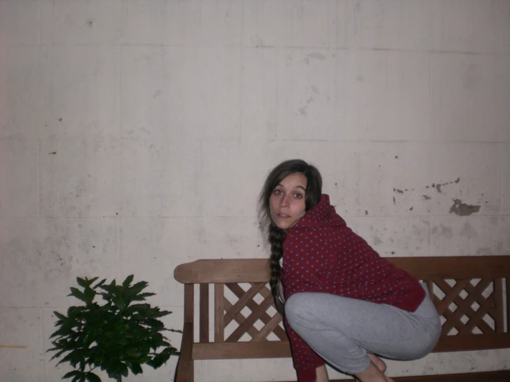 the woman poses on the bench beside the plant