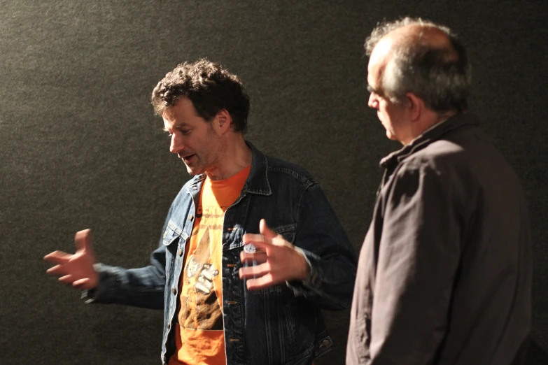 two guys looking at each other and one wearing an orange shirt