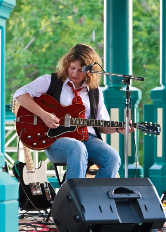 a woman sitting on the ground next to a microphone, playing guitar