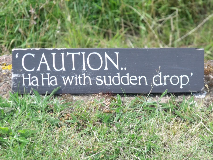the slate sign on a hill reads caution ha ha with sudden drop