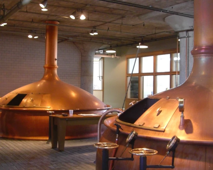 copper colored cooking pots in a factory with lighting and pipes