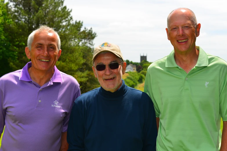 three men smiling for the camera next to trees