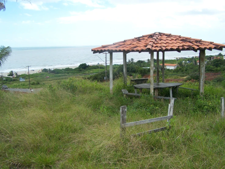 an umbrella made out of wooden poles in a grassy field next to the ocean